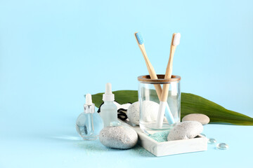 Toothbrushes with bottles of cosmetic oil, stones and palm leaf on blue background