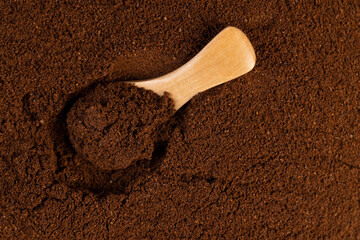 ground coffee and one spoon, a large number of roasted ground coffee beans in powder and a wooden spoon