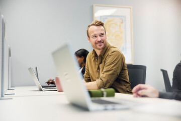 Smiling male corporate professional sitting with laptop at desk in office
