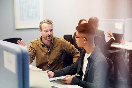 Male entrepreneur giving training to young employee writing notes while sitting in office
