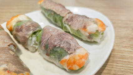 Eating delicious traditional food — Vietnamese fresh spring rolls: rice paper and vermicelli, vegetables, pork, seafood, lettuce, cucumber, herbs, shrimp, tangy fish sauce with lemon