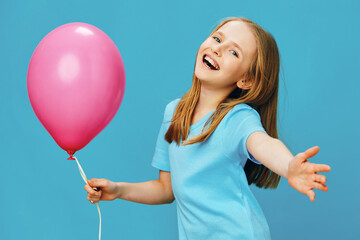 Happy young girl with long hair wearing a blue t shirt holding a pink balloon against a bright blue background, embodying joy and childhood innocence