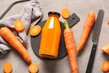 Board with bottle of fresh carrot juice on grey table