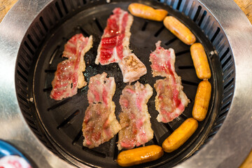Close up of pieces of yakiniku grilled Japanese wagyu beef and with sausage, charcoal fire in the stove