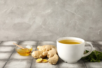 Cup of ginger tea and bowl with honey on grey tile table