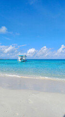 Fototapeta premium A pristine tropical beach scene with a single boat floating on incredibly clear, turquoise water under a bright blue sky. Idyllic natural beauty, perfect for a serene vacation or a tranquil escape
