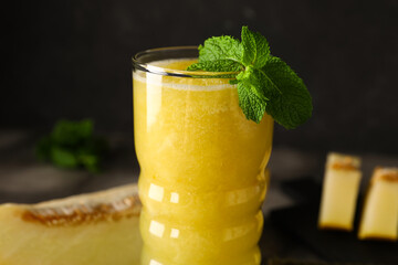 Glass of tasty melon smoothie with mint on black background