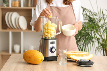 Woman preparing tasty melon smoothie at table in kitchen