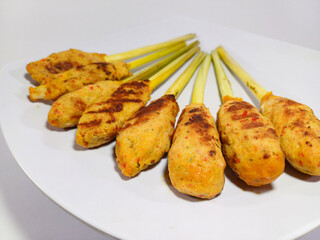 Several servings of Sate Lilit, an authentic, savory Indonesian dish consisting of minced meat (often fish or chicken) mixed with spices and wrapped around lemongrass stalks presented on a white plate