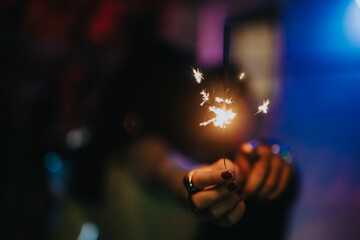 A close-up of a hand holding a sparkler, creating a warm festive atmosphere against a blurred colorful background.