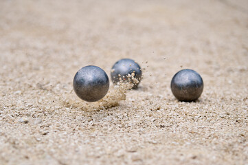 Flying petanque ball hits the ground, sending gravel into the air during a dynamic throw in a competitive match on a sandy terrain