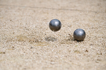 Flying petanque ball hits the ground, sending gravel into the air during a dynamic throw in a competitive match on a sandy terrain