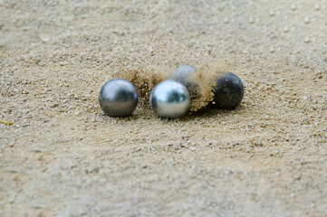 Close-up of petanque precision shooting moment with metal ball hitting target boule, sand and dust flying from impact on gravel court