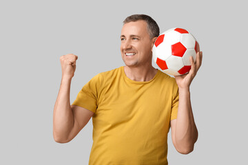 Happy handsome mature man with soccer ball on grey background