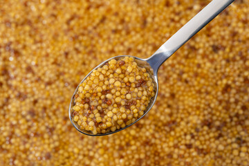 French Dijon mustard in a metal spoon, top view on mustard grains background. Gastronomy concept, organic food. Sauce. Slow rotation in a circle.