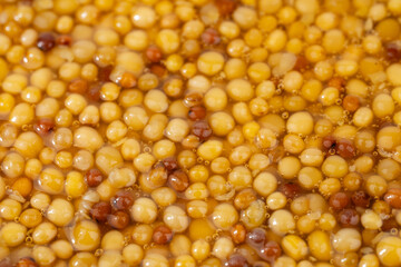 French Dijon mustard in a metal spoon, top view on mustard grains background. Gastronomy concept, organic food. Sauce. Slow rotation in a circle.