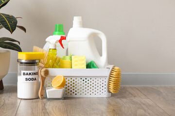 Basket with cleaning products on laminate floor against grey wall