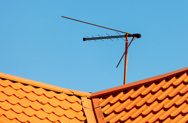 A television antenna is on top of a red roof