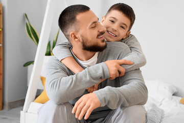 Happy father with his son in pajamas hugging on bed at home