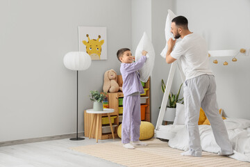Happy father in pajamas fighting pillows with his son at home