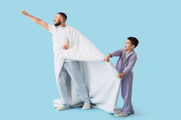 Happy father and his son in pajamas with blanket having fun on blue background
