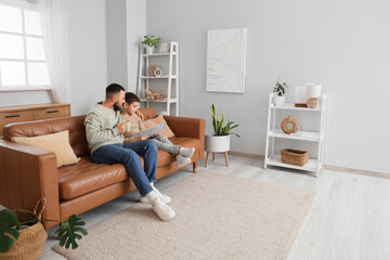 Happy father and his son with cup of tea reading book on brown leather sofa at home