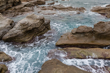Sea surf waves between coastal rocks in overcast rainy weather
