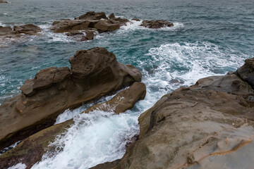 Sea surf waves between coastal rocks in overcast rainy weather