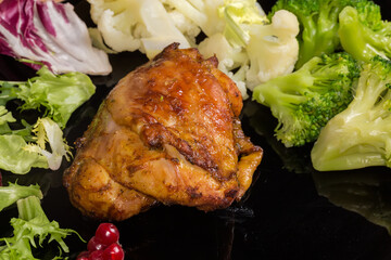 Baked chicken thigh among the vegetables on the black dish