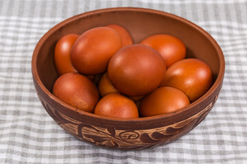 Several Easter eggs painted brown in clay bowl on tablecloth
