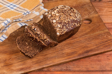 Partially sliced grain brown bread decorated with seeds and flakes