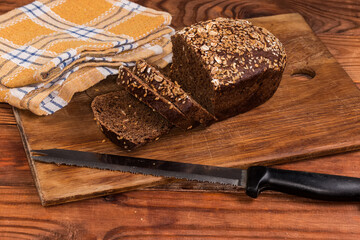 Partially sliced grain brown bread and serrated kitchen knife