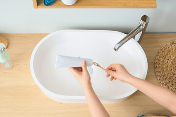Young woman applying toothpaste on brush near sink in bathroom, top view