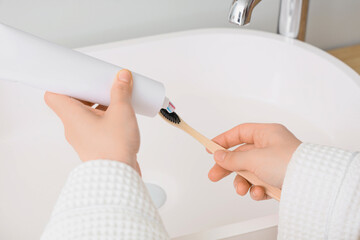 Young woman applying toothpaste on brush near sink in bathroom, closeup