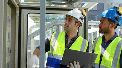 Two engineers in safety uniform checking building exterior power system at construction site rooftop, laptop in hand, sharing expertise in a moment of industrial collaboration, Worker maintenance - Powered by Adobe