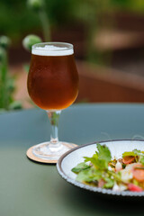 A glass filled with beer and a plate of salad next to it