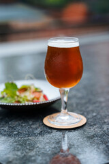 A glass filled with beer and a plate of salad next to it