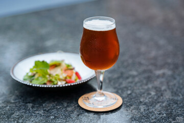 A glass filled with beer and a plate of salad next to it
