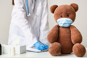 Female doctor with clipboard and toy teddy bear on table in clinic, closeup
