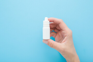 Young adult woman hand fingers holding and showing new white plastic bottle of medical liquid for eyes, nose or ears on light blue wall background. Pastel color. Closeup. Front view.