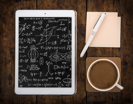 Tablet with mathematical and physical formulas, pen, notebook and cup of coffee on the table. Good background for design on the theme of Science, education.
