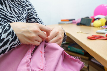 Sewing pink fabric at a crafting table with colorful tools and supplies in the background during a creative session