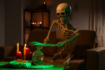 Skeleton with crystal ball and burning candles in dark living room
