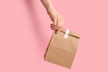 Female hand with paper bag on pink background. Food delivery service