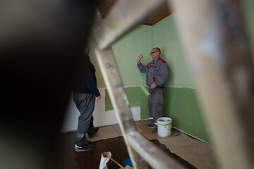 Two workers, dressed in work overalls, discuss in a room during the process of painting and...