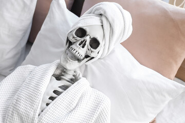 Human skeleton with towel and bathrobe lying in bedroom, top view