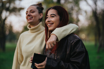 Two friends share a joyful moment outdoors, smiling and enjoying nature's calm atmosphere in a park.