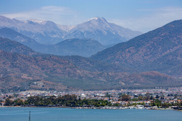 Obraz premium Panoramic view of Fethiye with waterfront, cityscape, and snow-capped Taurus Mountains under blue sky. Muğla, Turkey, Mediterranean region. Sunny spring day.