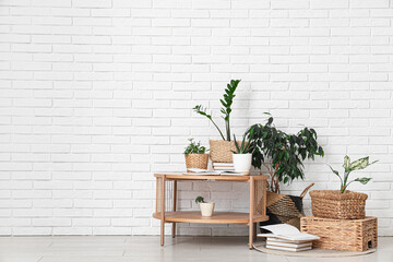 Table and wicker baskets with green plants near white brick wall in room