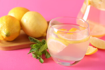 Glass of fresh lemonade with mint and lemons on pink background, closeup